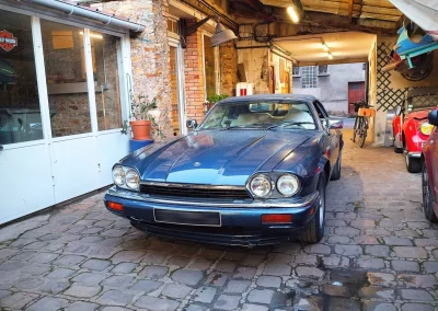 Jaguar XJS Cabriolet bleue dans l’entrée pavée du garage Autorosati