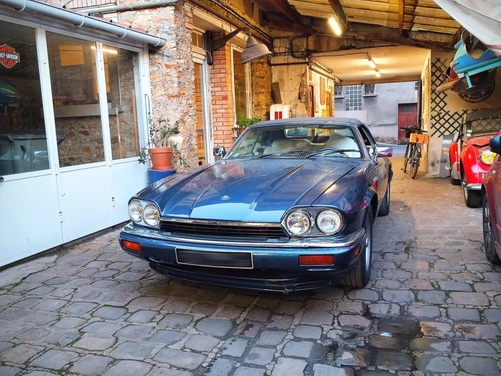 Jaguar XJS Cabriolet bleue dans l’entrée pavée du garage Autorosati