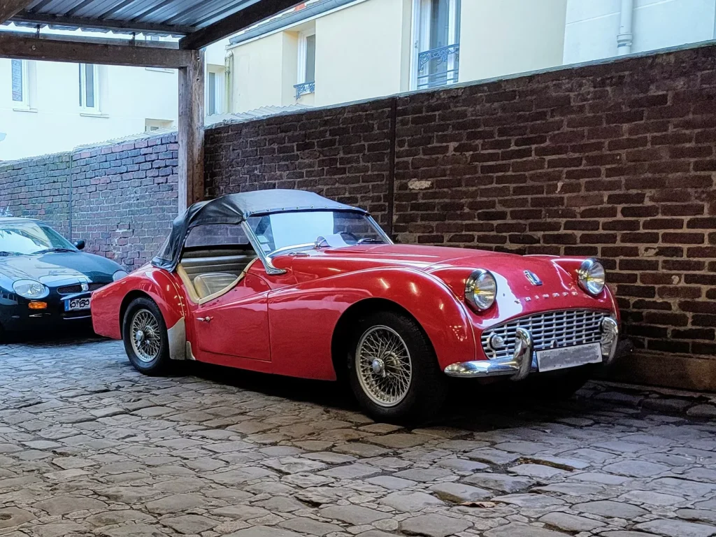 Triumph TR3 rouge devant le mur de brique du garage Autorosati